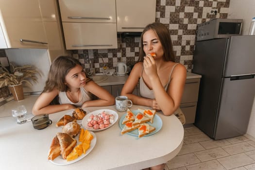 mom and daughter sitting at a table with a variety of food, including sandwiches, fruit, and pastries. They are smiling and enjoying their meal together