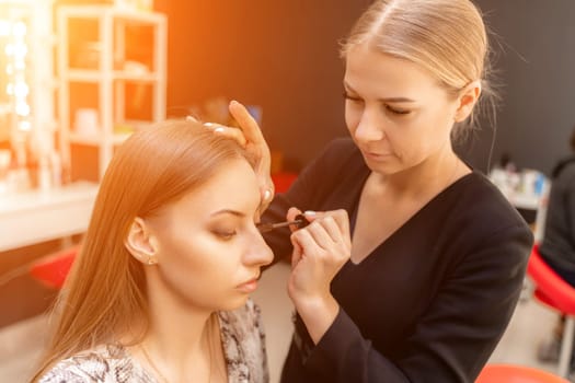 Makeup artist paints eyelashes to a woman in a beauty salon