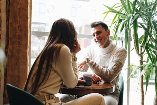 A man and woman are seated at a table engaging in conversation. They appear to be in deep discussion, leaning towards each other. The table is bare except for a few cups and plates. The man gestures with his hands while the woman listens intently.