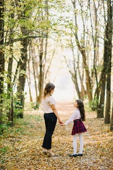 happy mom and daughter fall in the Park holding hands and smiling