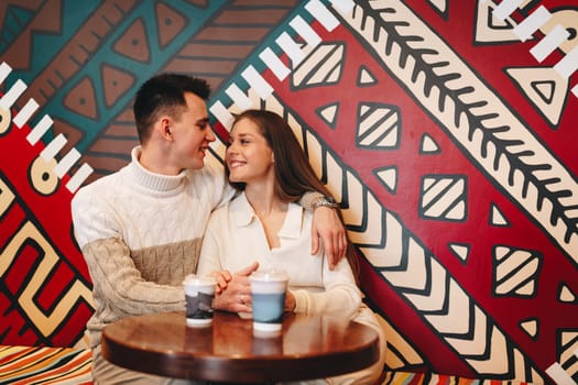 A man and woman are seated at a table placed in front of a vibrant and colorful wall. They appear engaged in conversation or perhaps enjoying a meal together.