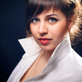 Young brunette girl in white shirt posing in Studio on black background