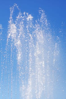 A liquid fountain spraying water against an electric blue sky, creating a stunning natural landscape with trees and clouds in the background