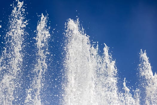 A liquid fountain spraying water against an electric blue sky, creating a stunning natural landscape with trees and clouds in the background