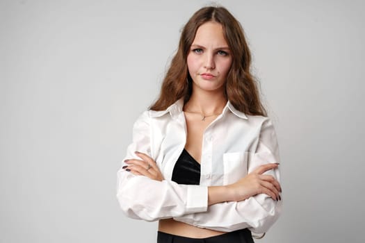 woman is standing wearing a white shirt and black pants. She has a confident stance and is looking directly at the camera.