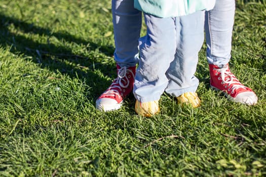 A person wearing jeans stood beside a child sporting red sneakers on their feet, showcasing a contrast in footwear choices