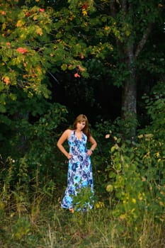 young Caucasian girl in blue dress posing in forest outdoors in summer