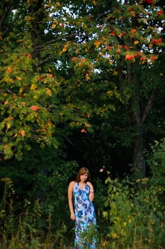 young Caucasian girl in blue dress posing in forest outdoors in summer