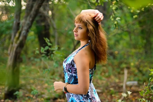 young Caucasian girl in blue dress posing in forest outdoors in summer