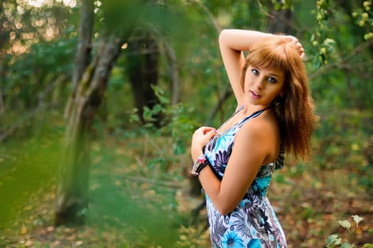 young Caucasian girl in blue dress posing in forest outdoors in summer