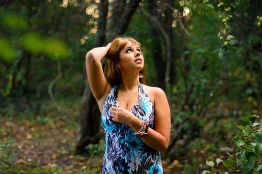 young Caucasian girl in blue dress posing in forest outdoors in summer