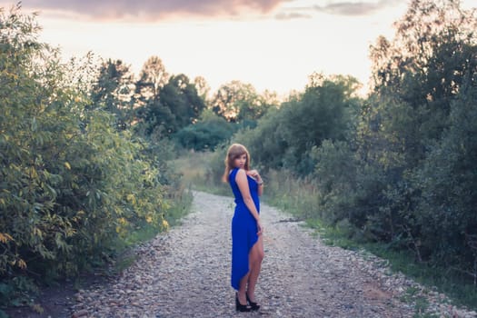 beautiful girl in blue dress posing on a background of sunset in nature