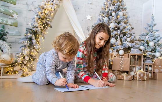 Children write a letter to Santa under the tree. Selective focus. Kid.