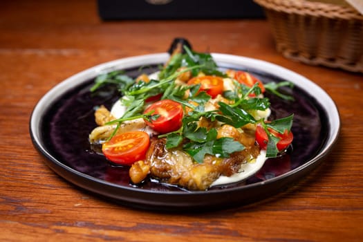 Salad with cherry tomatoes and herbs close-up on a black plate.