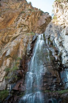 waterfall among the rocks. The mountain waterfall is surrounded by large cliffs and steep slopes.