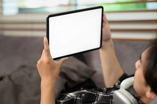 Man holding digital tablet with blank desktop screen lying on couch.