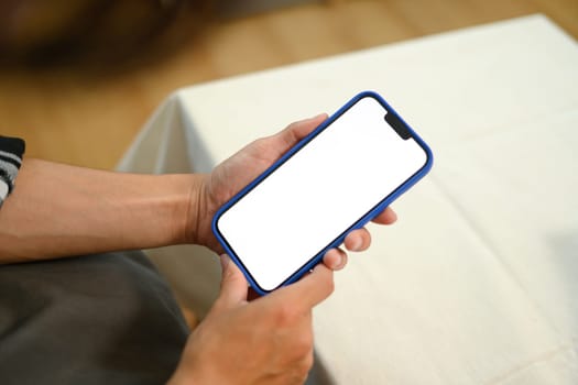 Unrecognizable man hands holding mobile phone with empty screen sitting on couch.