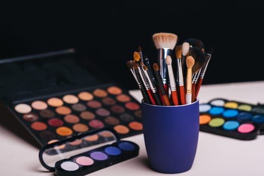 set of makeup brushes on the background of color eye shadow palette on the table