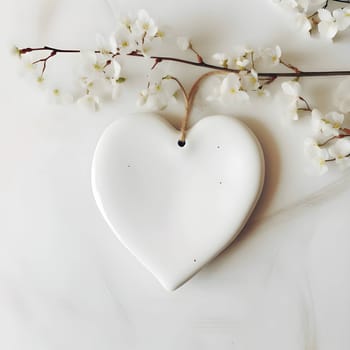 A white heart delicately suspended from a branch adorned with white flowers, radiating purity and grace.