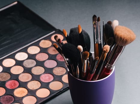 set of professional makeup brushes on a palette background with colored eye shadows on the table