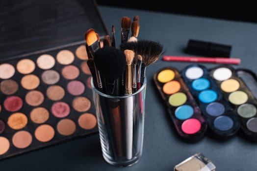 set of professional makeup brushes on a palette background with colored eye shadows on the table