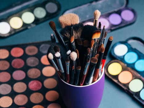set of professional makeup brushes on a palette background with colored eye shadows on the table