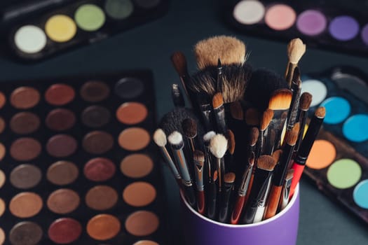 set of professional makeup brushes on a palette background with colored eye shadows on the table