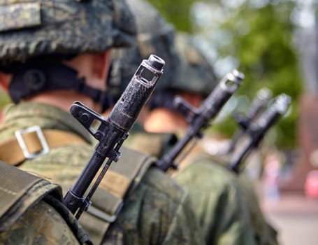 A soldier in full gear stands at attention with a rifle, wearing a helmet and camouflage uniform. Blurred background adds focus and determination to his readiness and vigilance.