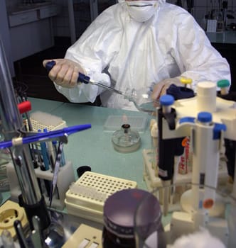 The scientist is meticulously working in a biosafety cabinet, wearing protective mask, gloves, and lab coat. Using a Bunsen burner, test tubes, and various lab equipment for experiments.