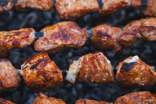 pork meat is cooked on skewers on barbecue grill close-up