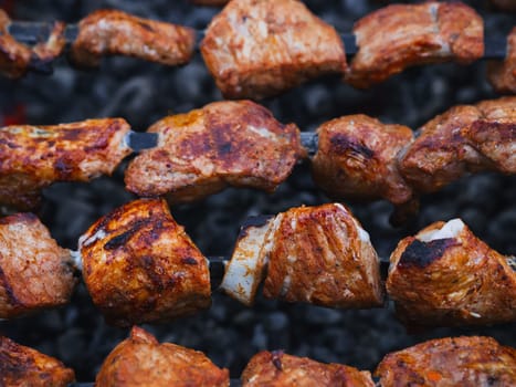 pork meat is cooked on skewers on barbecue grill close-up