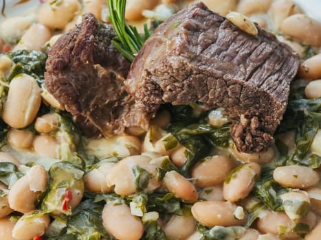 cooked beef in a sauce with beans and rosemary close-up