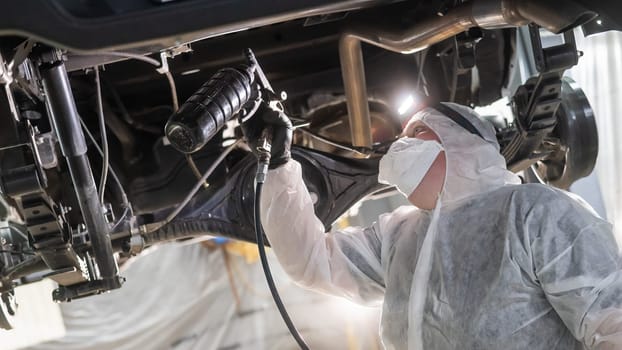 The master sprays an anti-corrosion compound on the bottom of the car