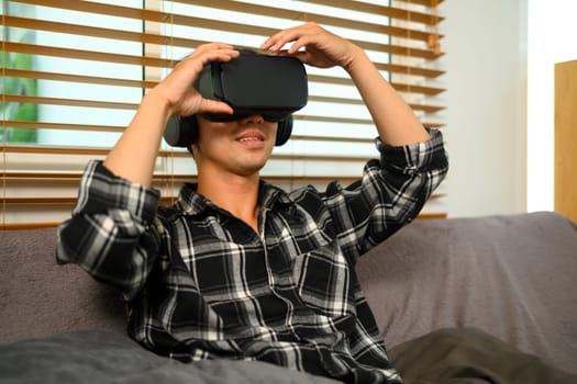 Young man virtual reality headset sitting on couch in living room.
