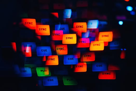 DJ mixer in a nightclub with a background of glowing lights from buttons and controllers