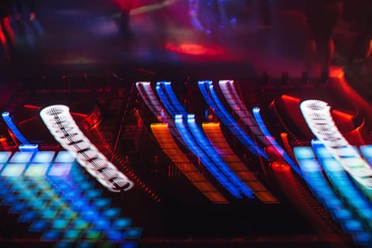 DJ mixer in a nightclub with glowing colored lights from controllers and buttons in the nightclub