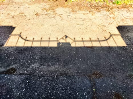 The shadow of the fence. Background, texture. Shadow of Ornate Fence Cast on Mixed Pavement at Midday. Contrast of shadow from an ornate fence