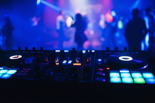 DJ mixer on the table background the night club and dancing people