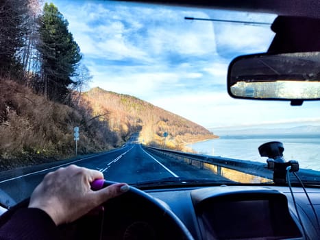 Car salon, windshield, hand of woman on steering wheel and landscape. View from seat of driver on nature landscape. Single trip of female traveler