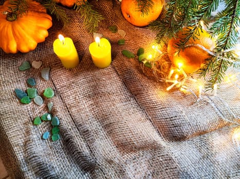 Festive decoration with bouquet and branches of spruce, bright glowing garlands and candles, burlap, oranges. Background for Christmas, New Year. Abstract texture, frame, place for text, copy space