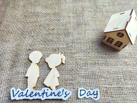 Wooden figurines of a couple, a house and the inscription Valentine's Day. The concept of a holiday of love and lovers. Background, texture, place for text and copy space