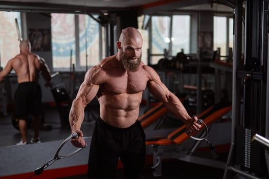 Bald Caucasian bodybuilder training chest using cable crossover in gym
