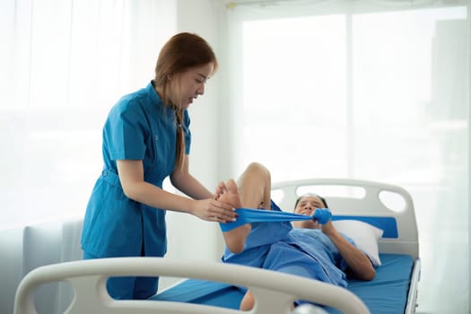 A woman in a blue uniform is helping a man with a cast on his foot. The woman is holding a blue bandage and the man is lying on a hospital bed. Scene is one of care
