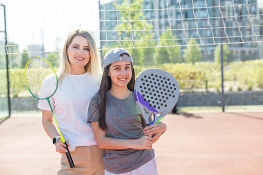 Happy caucasian mother and daughter playing padel tennis and badminton on tennis court outdoors. High quality photo