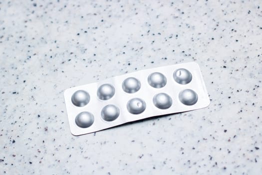 A blister pack of pills sits on a counter top, the circular design and metallic aluminum material creating a modern fashion accessory. The font on the packaging hints at the chemical compounds inside