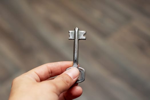 The person is holding a small key, made of nickel and metal, resembling a fashion accessory or possibly a religious item. It is small enough to fit in the palm of their hand