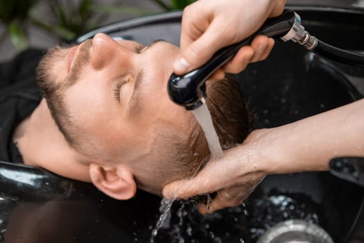 Skilled hairstylist tenderly rinses a clients hair with warm water in barbershop.