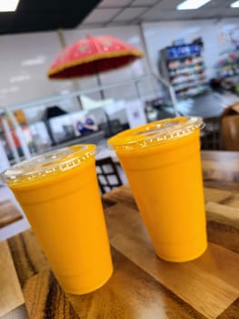 Vibrant Indian Mango Lassi drinks on a wooden table in a lively, modern fast food restaurant with quirky decor.