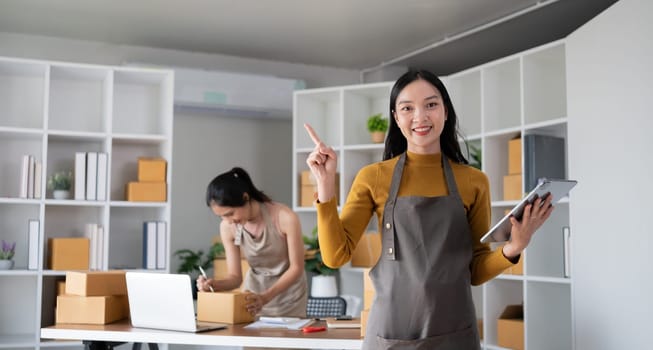 Smiling young woman in warehouse holding tablet with colleague working in background..