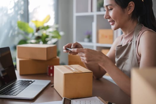 Smiling young woman in warehouse scanning package with smartphone.